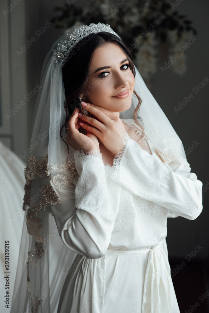 Preparing the bride for the upcoming wedding. Beautiful bride dresses earrings. Beautiful bride with stylish make up and hair style. Sexy bride. Bride's preparation at home before the wedding ceremony Preparing the bride for the upcoming wedding. Beautiful bride dresses earrings. Beautiful bride with stylish make up and hair style. Sexy bride. Bride's preparation at home before the wedding ceremony