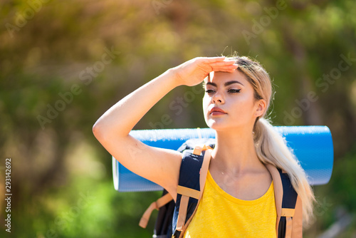 Teenager girl hiking at outdoors looking far away with hand to look something