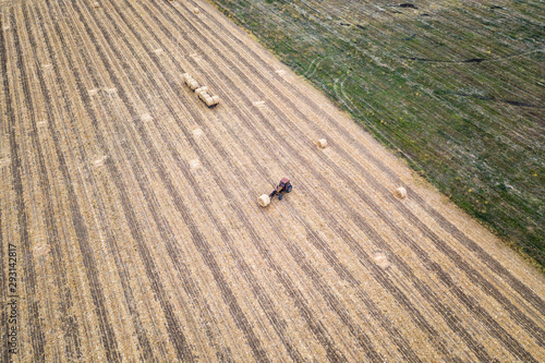 Aerial view from drone to the tractor collect bales of hay after harvesting on a wheat field.