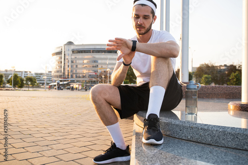 Young athlete in windrunner sitting on the street after good jogging session at sunset. photo