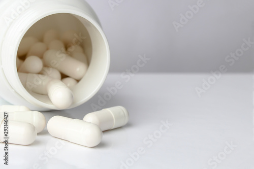 White pills from a white jar on a light background. Professionally photo with place for text