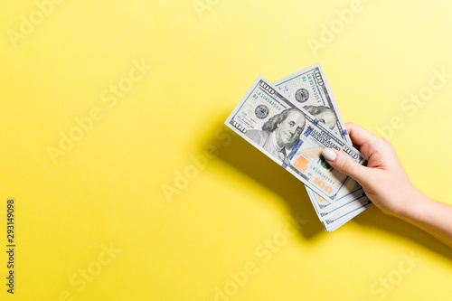 Female hand holding a bundle of money on colorful background. Top view of one hundred dollar banknotes. Salary concept with empty space for your design