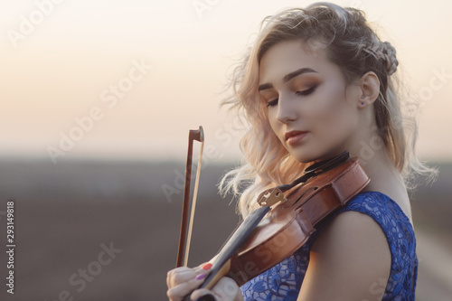 portrait of a romantic young woman with a violin under her chin outdors, girl face relaxing in solitude with music on nature, concept hobby and lifestyle