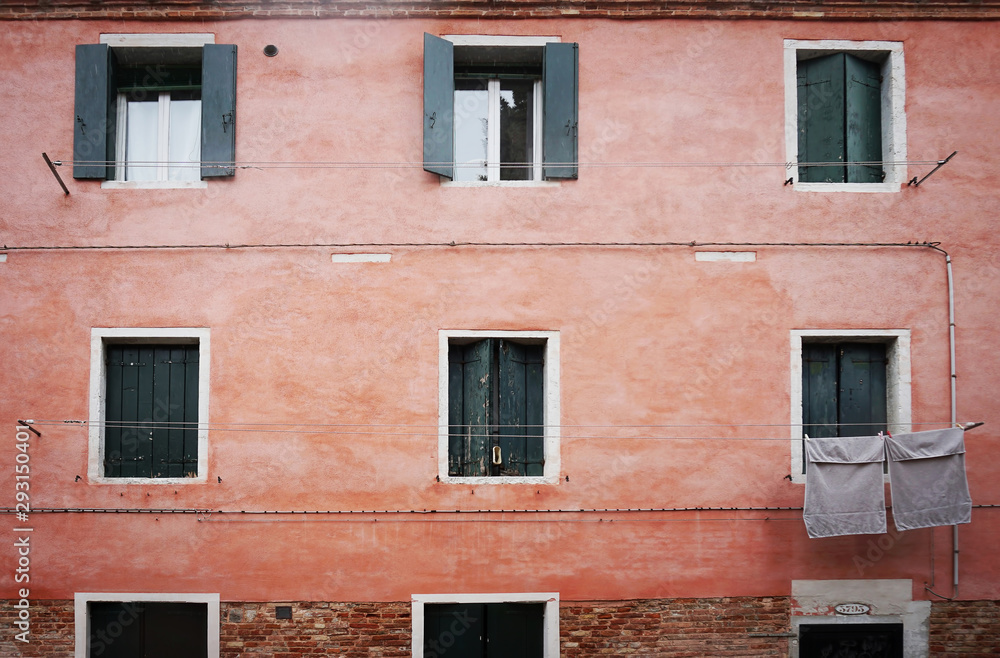 In Venice. View of a pink wall with windows with shutters and drying rags on a rope