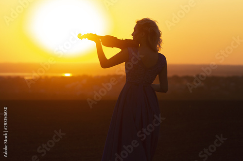 silhouette of a female figure in a long dress playing the violin on a natural background, woman relaxing in music