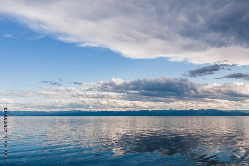 white clouds over the wavy surface of a blue lake. mountains on the other side of Lake Baikal