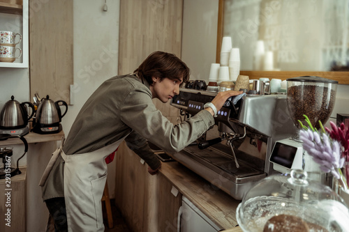 Responsible young barista cleaning the coffee machine