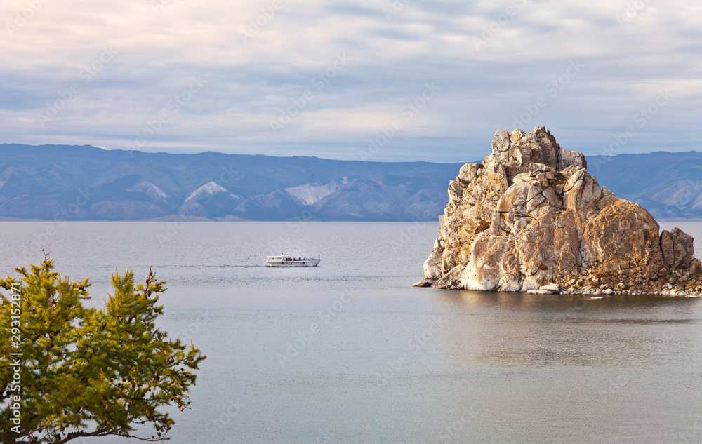 Baikal Lake. Tourists travel on a pleasure boat along the island of Olkhon and explore the natural attraction Shamanka Rock in a warm September evening