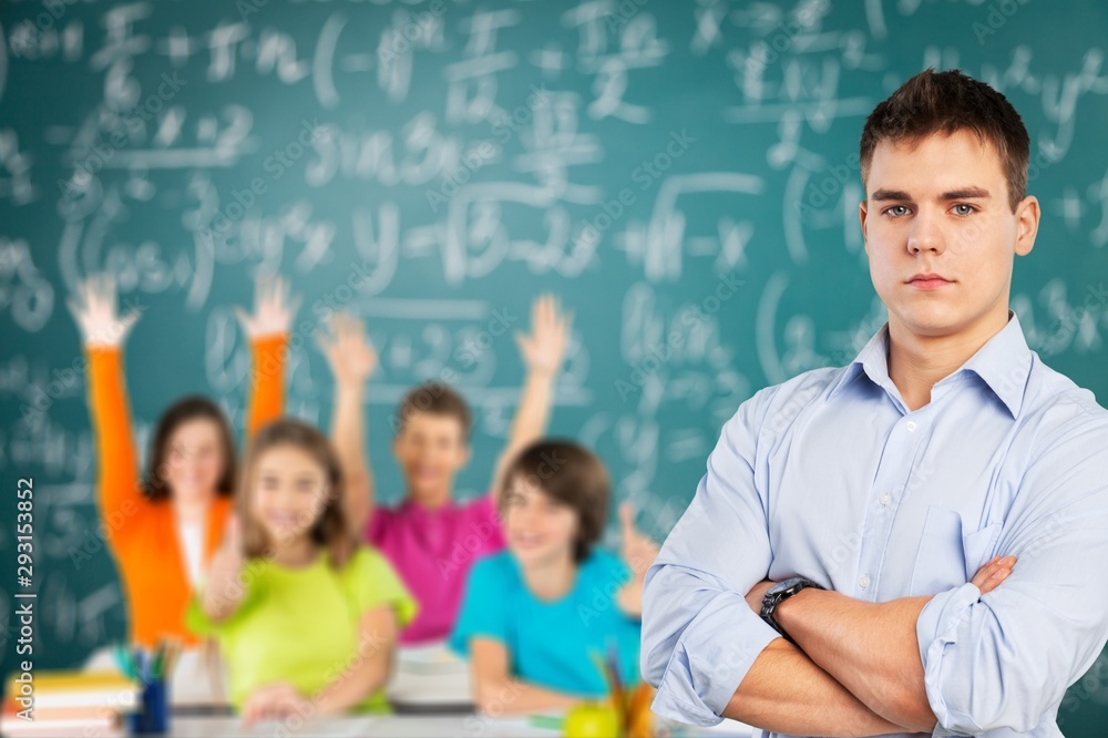 Young male teacher standing with the watch on classroom background