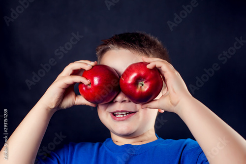 A portrait of a boy holds apples like eyes in front of dark background. Children and food concept