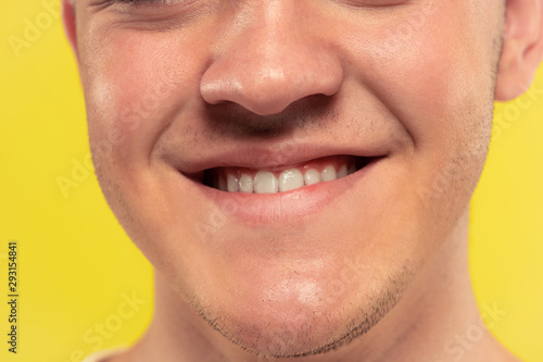 Caucasian young man's close up portrait on yellow studio background. Beautiful model with well-kept skin. Concept of human emotions, facial expression, sales, ad. Lips and cheeks, smiling with teeth.