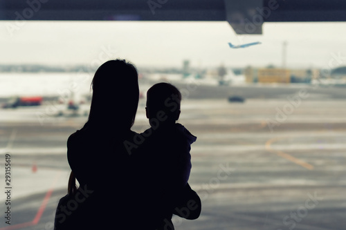 Photography Silhouette of mother holding on hands little toddler boy with window of airport on background