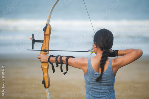 Fotografie, Obraz Asian Archery woman with bow shooting on the beach
