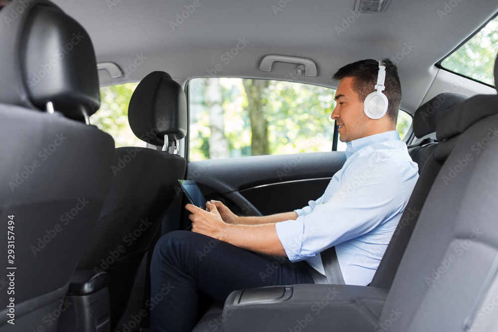transport, business and technology concept - male passenger or businessman with wireless headphones using tablet pc computer on back seat of taxi car transport, business and technology concept - male passenger or businessman with wireless headphones using tablet pc computer on back seat of taxi car