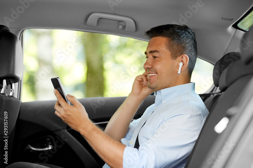 transport, business and technology concept - smiling male passenger or businessman with wireless earphones using smartphone on back seat of taxi car © Syda Productions