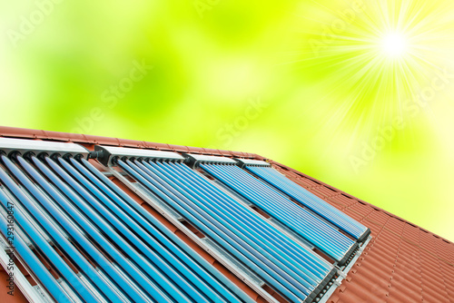 Vacuum collectors - solar water heating system on red roof house with green spring sun background photo