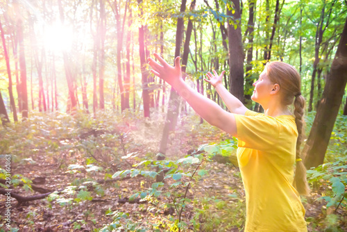 Happy young pretty woman outstretching hands to sun light in forest