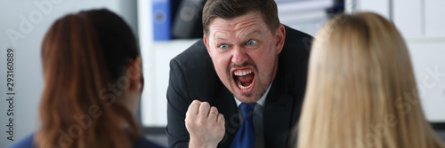 Portrait of screaming businessman angrily looking at guilty business worker made important mistake. Serious male standing in big modern corporate cabinet. Blurred background