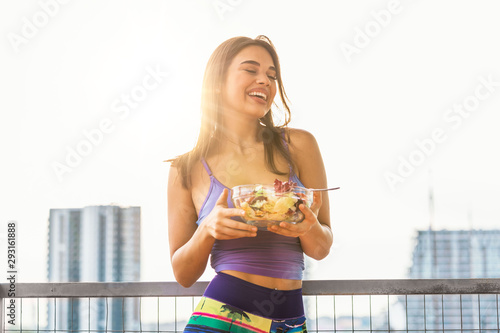 Young and beautiful woman enjoying heathy salad with sunshine behind her. Healthy food concept Beautiful fit woman eating healthy salad after fitness workout