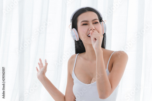 Beautiful woman wearing white headphones, Raise your hand to sing happy in bright white bedroom morning