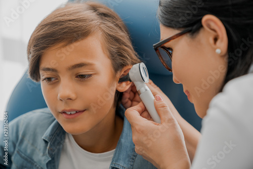 Female doctor examining boy's ear with otoscope photo