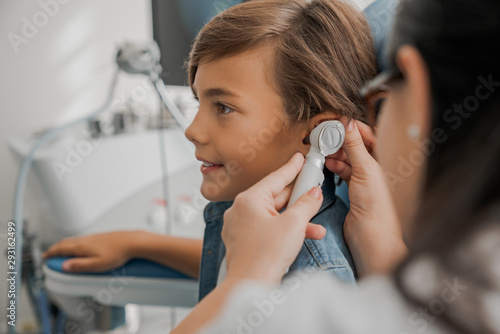 Side view shot of female doctor examining boy's ear with otoscope photo