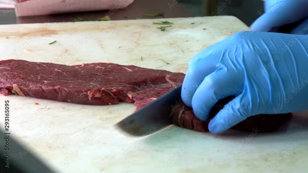 A butcher slicing raw meat on plastic board on the table A butcher slicing raw meat on plastic board on the table