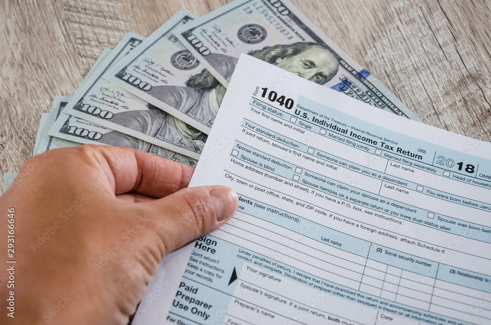Fototapeta premium tax form 1040 in a hand on a background of dollars. Close-up.