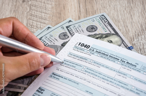 female hand fills tax form 1040, dollars on a wooden table. Close-up. Business concept.