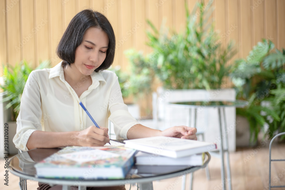 Young beautiful Asian woman reading a book while doing her homework in the modern co working space Young beautiful Asian woman reading a book while doing her homework in the modern co working space