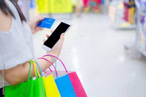 Close up woman hand holding phone, shopping bag and credit card in the shopping mall. Shopping concept.