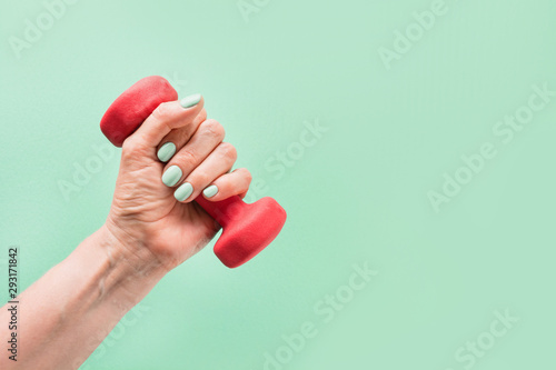 Female hand with red dumbbell on green background. Sport fitness equipment.