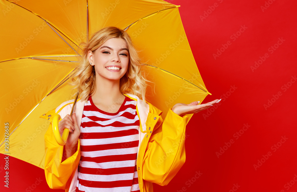 young happy emotional cheerful girl laughing and jumping with yellow umbrella   on colored red background. - obrazy, fototapety, plakaty 
