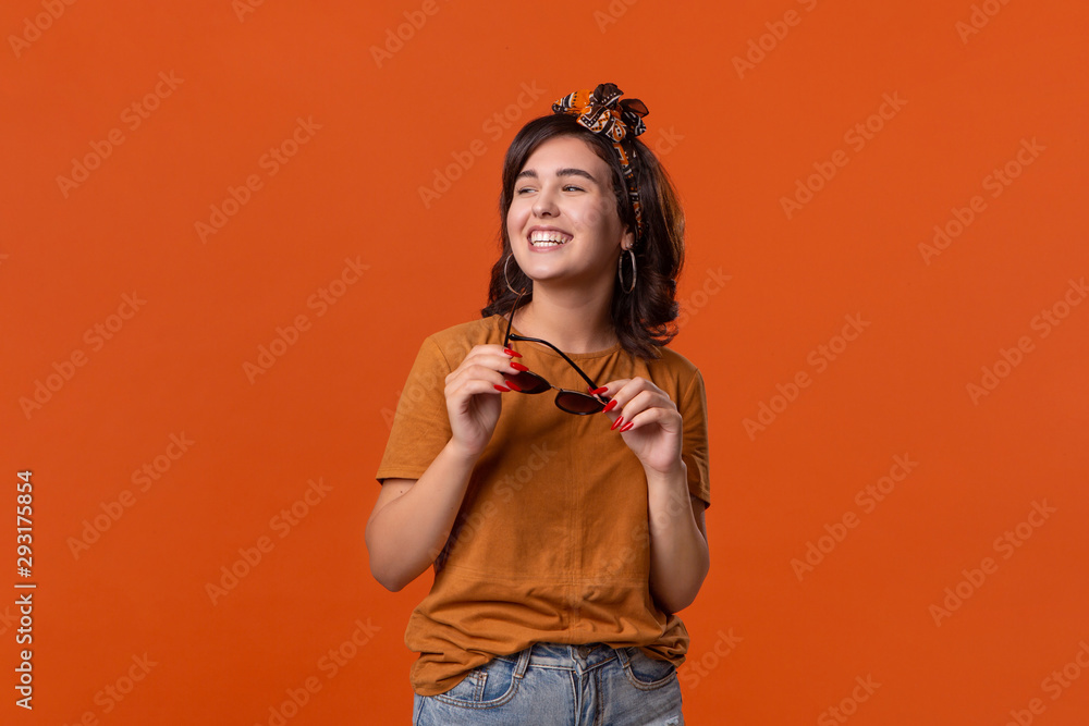 Pretty brunette woman in a t-shirt and beautiful headband and sunglasses posing isolated over orange background. Pretty brunette woman in a t-shirt and beautiful headband and sunglasses posing isolated over orange background.