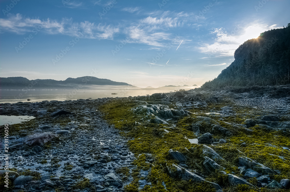 Obraz premium Golden morning as the sun rises above the rocks reflecting over the low tide, St-Lawrence river shore, Quebec, Canada