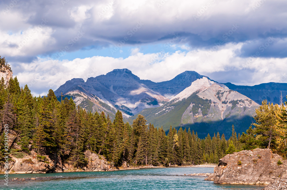 The Bow river in Banff National Park in Alberta, Canada on a sunny fall day under blue skies and white clouds with a mountain range in the background The Bow river in Banff National Park in Alberta, Canada on a sunny fall day under blue skies and white clouds with a mountain range in the background