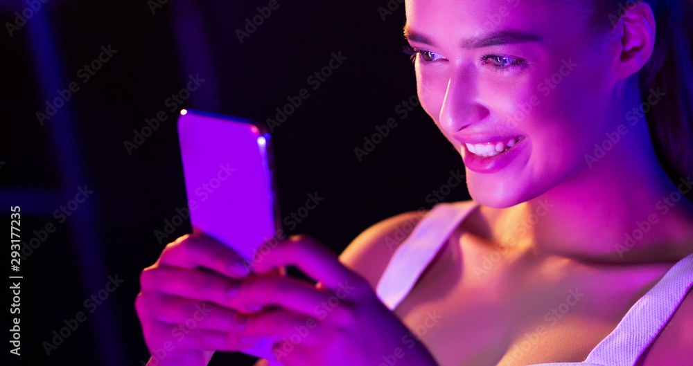 Fototapeta Girl surfing internet on phone in pink neon light