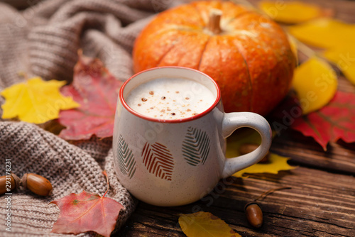 Pumpkin spiced latte or coffee in glass decorated knitted scarf on turquoise vintage background. Autumn, fall or winter hot drink. Cozy breakfast.