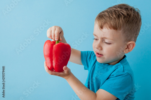 Little kid holding pepper in his hands on blue background. Vegan and healthy concept