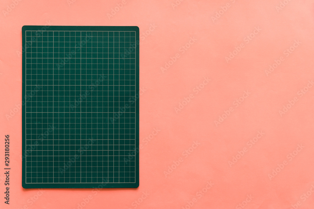 Top view of green rubber cutting mat on the left side over pink color paper background. Background with copy space. Top view of green rubber cutting mat on the left side over pink color paper background. Background with copy space.