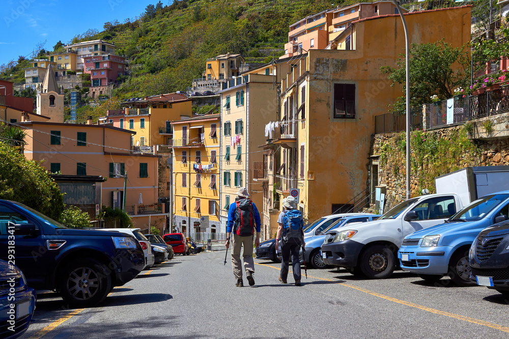 Happy couple of tourists, a man and a woman with backpacks walking along the historical part of the city RIomaggiore, Italy. Back view. Travel to Europe, vacation.