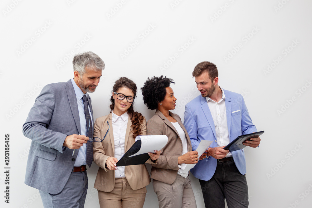 Group of four multiethnic business people standing in front of white wall Group of four multiethnic business people standing in front of white wall