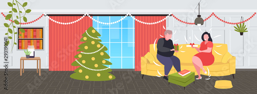 fat overweight couple giving surprises gift boxes to each other obese man woman sitting on couch holiday celebration obesity concept modern living room interior horizontal flat full length