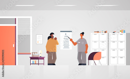 female doctor ophthalmologist pointing at letters on eye chart checking african american patient vision medicine healthcare concept hospital medical clinic office interior full length horizontal