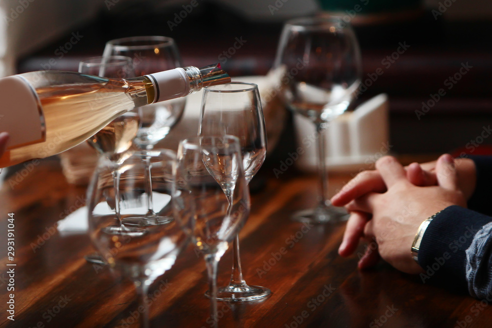 Bottle with wine and wine glasses on the table. Wine tasting. Male hands and the hands of a waiter. Wine is pouring into a glass. Out of focus. Photo without a face.