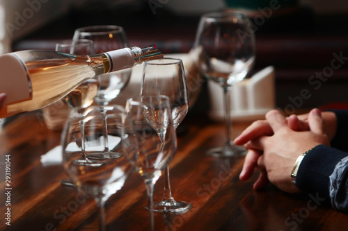 Bottle with wine and wine glasses on the table. Wine tasting. Male hands and the hands of a waiter. Wine is pouring into a glass. Out of focus. Photo without a face.