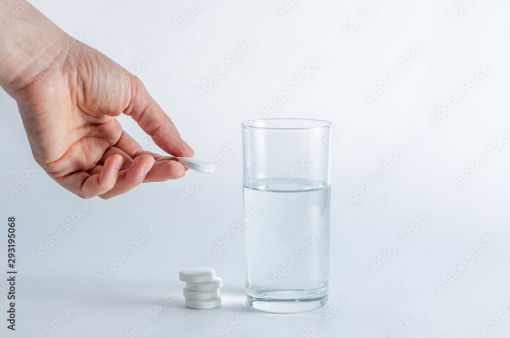 A hand holds an effervescent soluble tablet and places it in a glass of water. Isolated on white background. The concept of treatment and prevention of viral diseases. Help for depression and insomnia A hand holds an effervescent soluble tablet and places it in a glass of water. Isolated on white background. The concept of treatment and prevention of viral diseases. Help for depression and insomnia