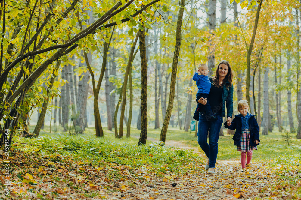Mom with daughter and son are walking in the autumn park. Family for a walk in the forest