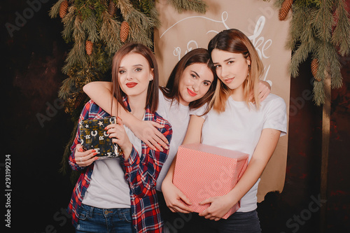 Three beautiful girls in a photo studio. Women near Christmas tree. Ladies in a white t-shirts