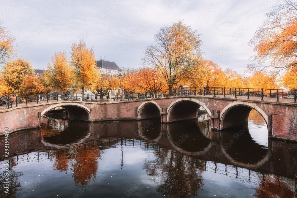 Amsterdam canal with its bridges in beautiful fall colors in the old center of Amsterdam with the silhouette of the Amsterkerk in the background